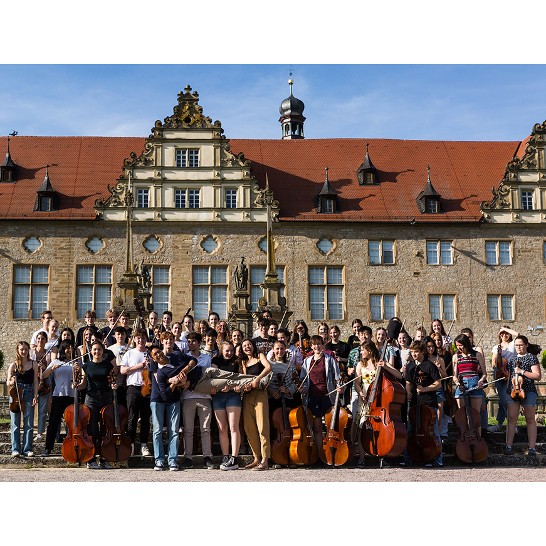 Jugendliche des Orchester stehen vor dem Schloss und tragen Herrn Adiarte