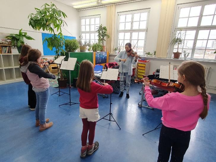 Eine Geigenlehrerin spielt mit ihren 4 Schülerinnen Geige.