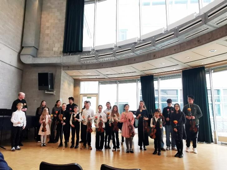 Kinder stehen mit Ihren Violinen und einer Rose in der Hand nebeneinander