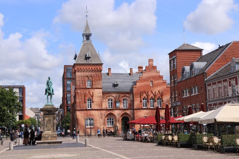 Der Marktplatz der Stadt Esbjerg. Ein rotes Backsteingebäude und große Sonnenschirme sin am Marktplatk
