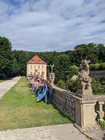 mehrere Kinder lehnen mit ihrer rechten Seite und dem Rücken zum Betrachter an einer Mauer und strecken ihr linkes Bein und ihren linken Arm nach links