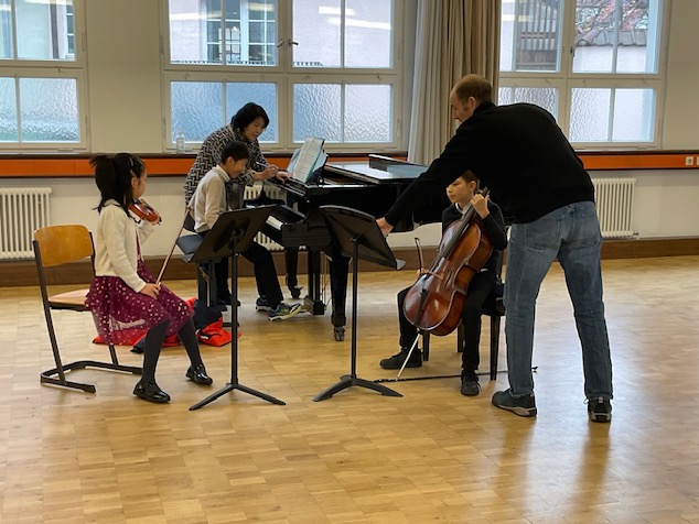 drei Schüler mit Geige, Klavier und Cello und zwei Lehrkräfte